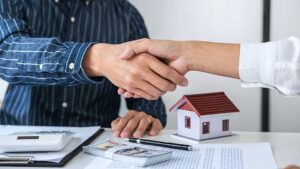 A couple reviews property documents with a real estate agent at a kitchen table.